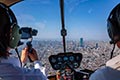 大阪平野をヘリコプター機内でスマートフォンを使用して撮影している男性の後ろ姿
